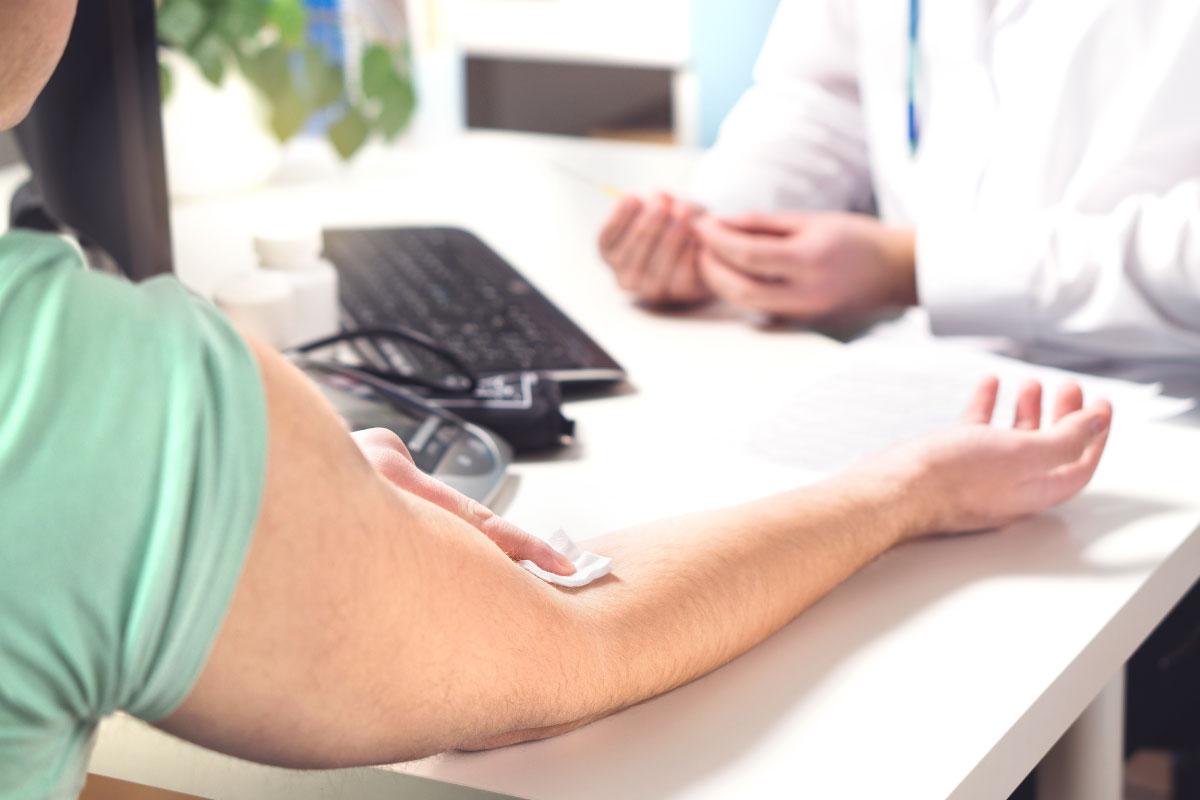 Physician with an individual holding gauze on his inner elbow in a office